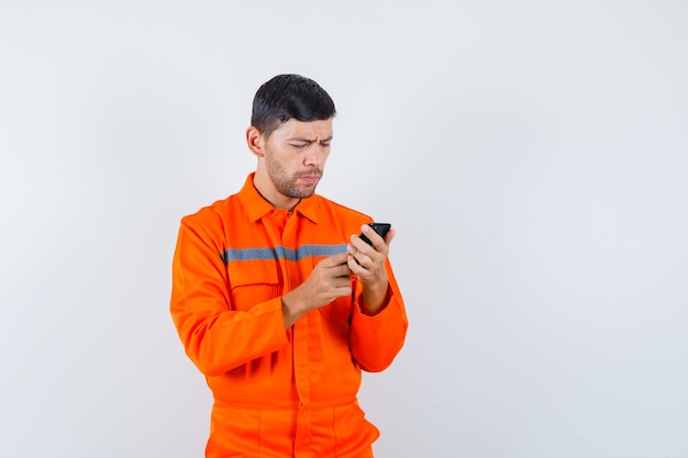 Industrial man using mobile phone in uniform and looking busy , front view.