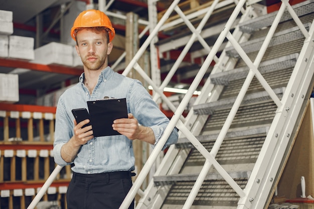 Industrial worker indoors in factory. Businessman with orange hard hat. Man in a blue shirt.