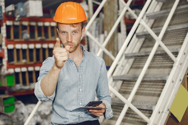 Industrial worker indoors in factory. Businessman with orange hard hat. Man in a blue shirt.