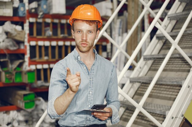 Industrial worker indoors in factory. Businessman with orange hard hat. Man in a blue shirt.