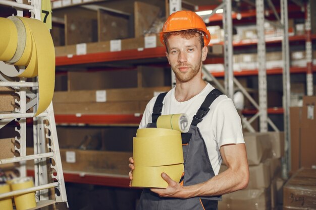 工場の屋内の産業労働者。オレンジ色のヘルメットをかぶった若い技術者。