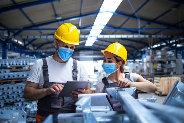 Industrial workers with face masks protected against corona virus discussing about production in factory