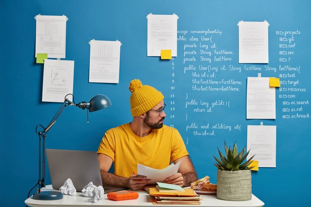 Inexperienced European man looks through paper documents, analyzes during working process