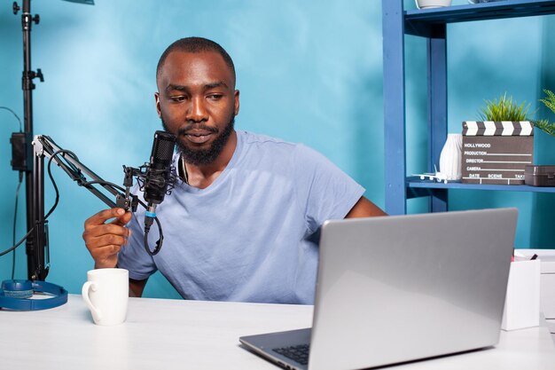 Influencer reading questions from followers received in live session on laptop screen using professional microphone in vlogging studio. Vlogger giving feedback to followers.