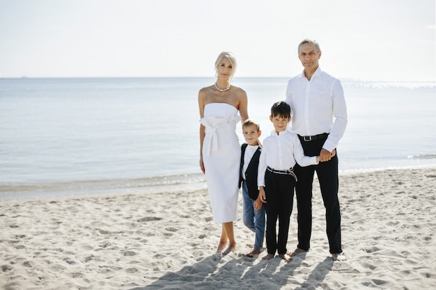 Informal family portrait on the sand beach on the sunny summer day, of parents and two sons dressed in formal attires