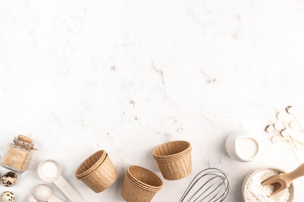 Ingredients For Baking cupcakes on a white concrete background. Flour, Eggs, cane sugar, red whisk, milk, spices in measuring spoons, muffin molds. Space For Copying The Top View.