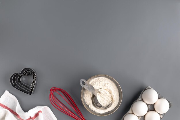 Ingredients for baking on a dark gray background flour eggs butter heart shape whisk textiles