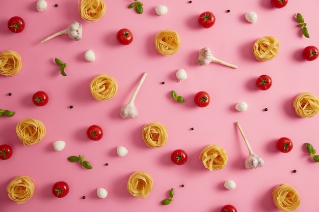 Ingredients for cooking pasta. Above shot of homemade round pasta balls fettuccine, tomatoes, garlic, basil and mozzarella cheese on pink background. Selective focus. Culinary. Fresh products