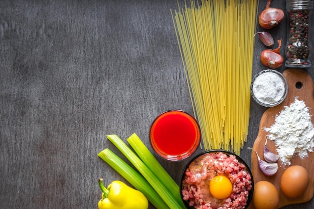 Ingredients for cooking pasta. Spaghetti, tomato juice, olive oil, garlic, minsed meat, pepper and fresh celery on wooden background, top view, copy space