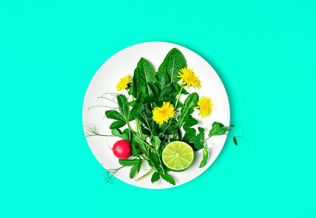 Ингредиенты для свежего зеленого салата с одуванчиками и съедобными цветами на тарелке