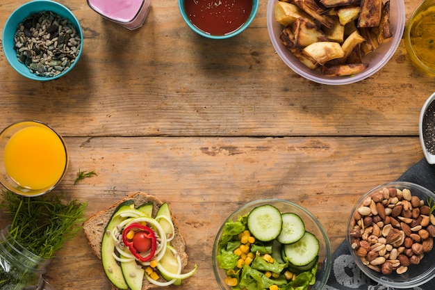 Ingredients; juice; dryfruits; roasted potato; smoothie; sandwich and oil arranged on wooden table