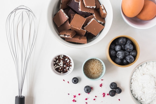 Free photo ingredients for making cake with whisk on white background