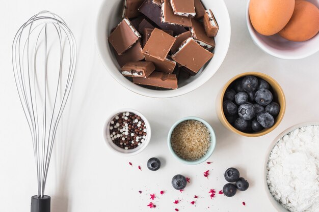 Ingredients for making cake with whisk on white background