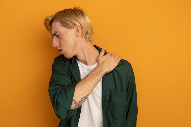 Free photo injured young blonde guy wearing green t-shirt grabbed aching shoulder