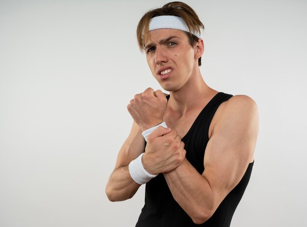 Injured young sporty guy wearing headband and wristband grabbed aching wrist isolated on white wall with copy space