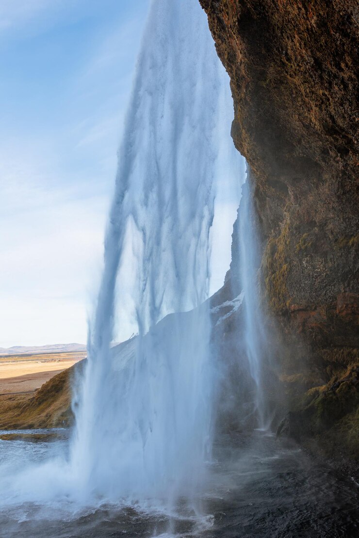 Free Photo inside arctic skgafoss waterfall with river stream frunning down off mountain edges, icelandic cascade with water flow falling. scandinavian nature and wilderness, beautiful landscape.