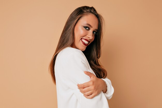 Inside portrait of smiling happy european woman with wine lips wearing white jacket posing at camera