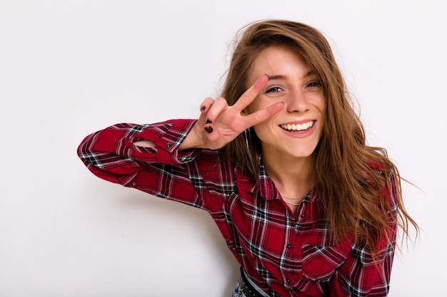 Inside portrait of young pretty lady with long brown hair wearing stripped shirt posing with peace sign over isolated white wall,