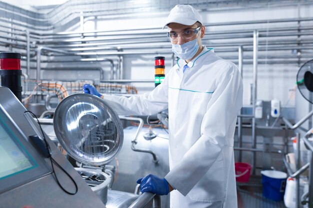 Inspector in a mask and a scrub stands with a foldertablet in his hands at the dairy plant