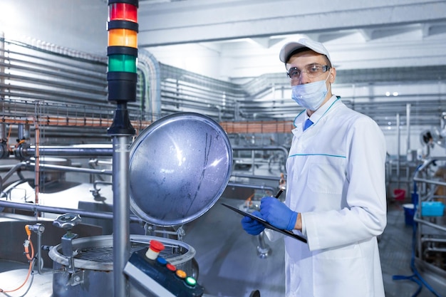 Inspector in a mask and a scrub stands with a foldertablet in his hands at the dairy plant