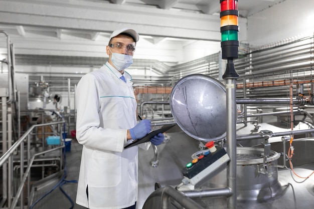 Inspector in a mask and a scrub stands with a foldertablet in his hands at the dairy plant