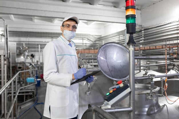 Инспектор в маске и скрабе стоит с папкой в руках на молочном заводе