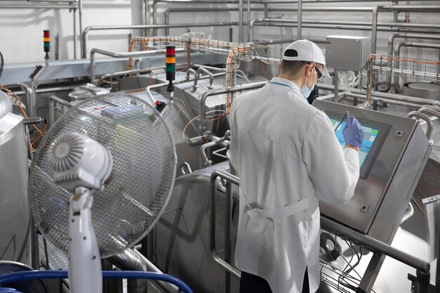 Inspector in a mask and a scrub stands with a foldertablet in his hands at the dairy plant