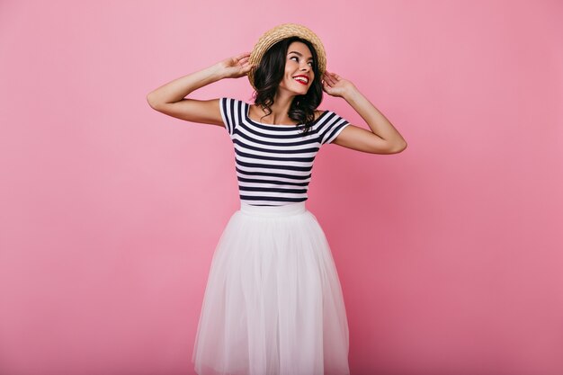 Inspired brunette girl in summer hat chilling. Tanned lovable woman in white skirt having fun.