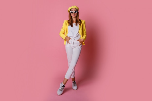 Inspired brunette woman in yellow jacket and beret jumping on pink