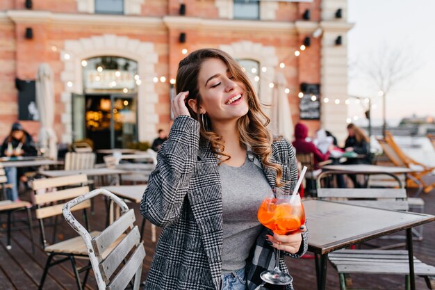 Inspired caucasian lady plays with her brown hair and tasting fruit cocktail