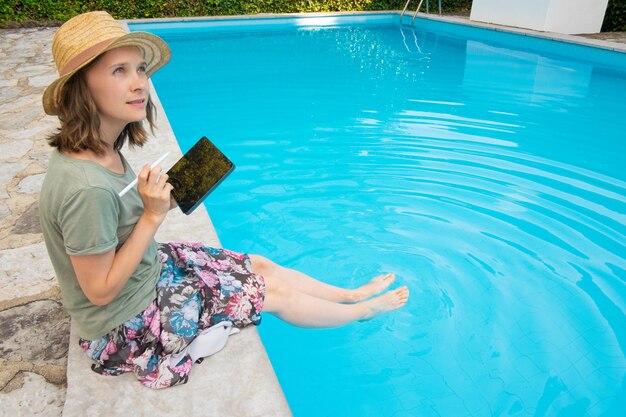 Inspired creative woman in summer hat sitting at poolside