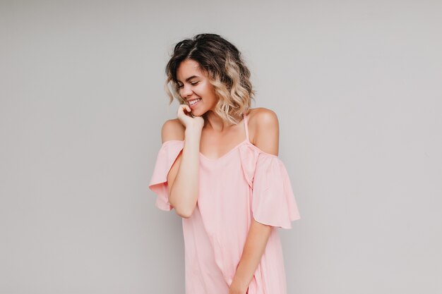 Inspired european girl in stylish attire posing with shy smile. Portrait of enchanting white lady wears pink dress.