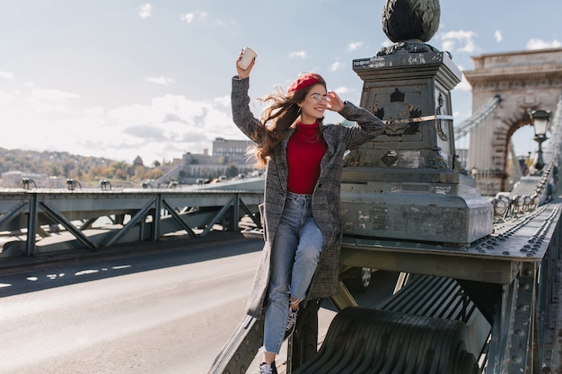 Inspired female model wears vintage jeans relaxing during photoshoot on bridge