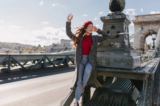 Inspired female model wears vintage jeans relaxing during photoshoot on bridge