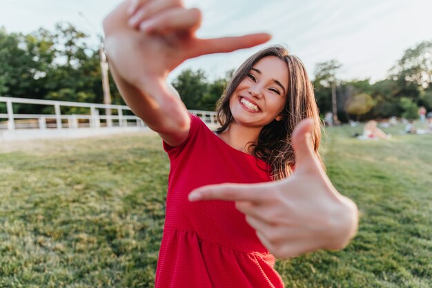 陽気な笑顔で踊るインスピレーションを得たハンサムな女性。屋外の写真撮影を楽しんでいる壮大な黒髪の少女。