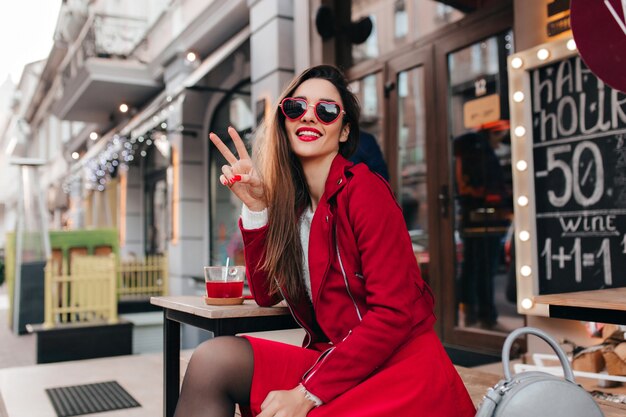 Inspired lady in trendy red skirt making peace sign