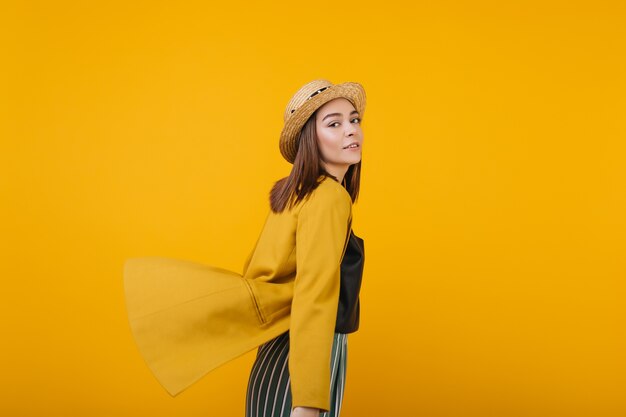 노란색 재킷 포즈에서 영감을받은 아가씨. 밀짚 모자에 평온한 여성 모델의 실내 사진.