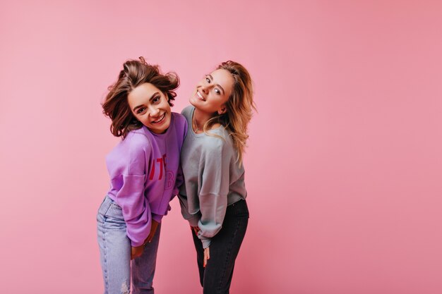 Inspired woman in purple shirt having fun with best friend. Indoor portrait of two amazing ladies in casual outfit.