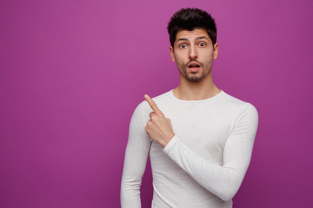 Inspired young handsome man looking at camera pointing up on purple background with copy space