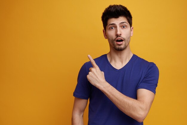 Free photo inspired young handsome man looking at camera pointing up on yellow background with copy space