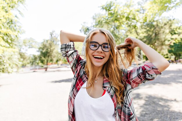 Inspired young woman smiling in warm spring day. Summer portrait of interested blonde girl in glasses.