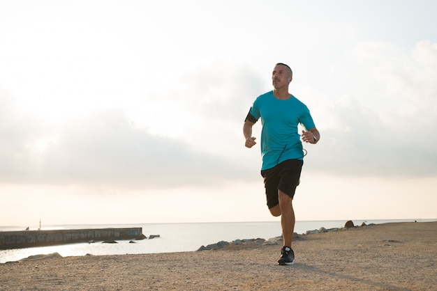 Inspirited handsome sportsman running over beach