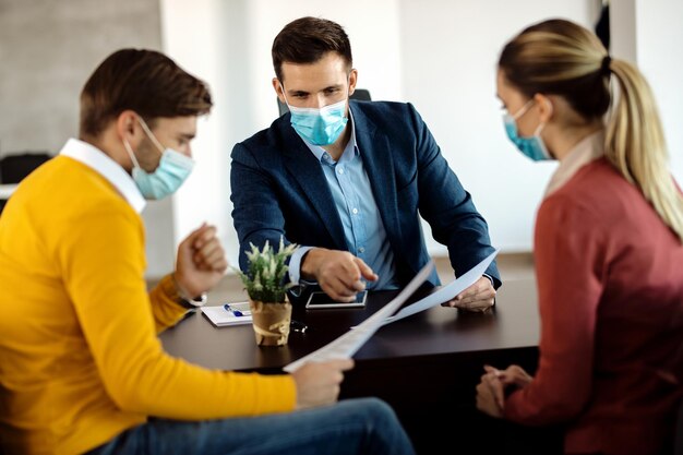 Insurance agent and a couple analyzing documents while wearing protective face masks during the meeting