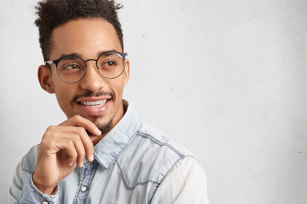 Intelligent clever male student wears round spectacles, thinks over future project,