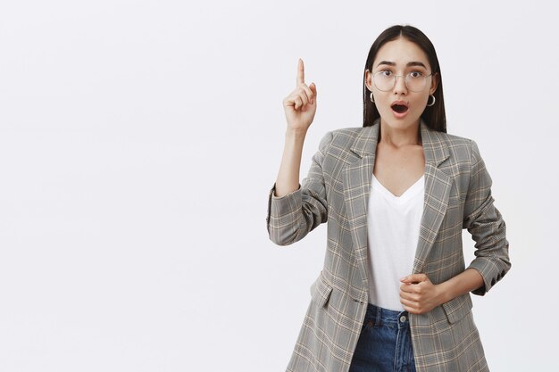 Intense thrilled adult female in glasses and jacket, lifting index finger in eureka gesture, gasping, saying interesting thought