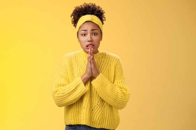 Intense worried perplexed young gloomy african-american woman hold hands pray frowning cringing begging favour standing troubled bad situation need help forgiveness feel awkward, yellow background.