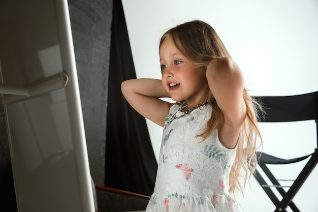 Free photo interaction of children with adult world. cute girl wearing accessories for being older, looking playful, happy. little female model trying on mum's jewelry at home. childhood, style, dream concept.