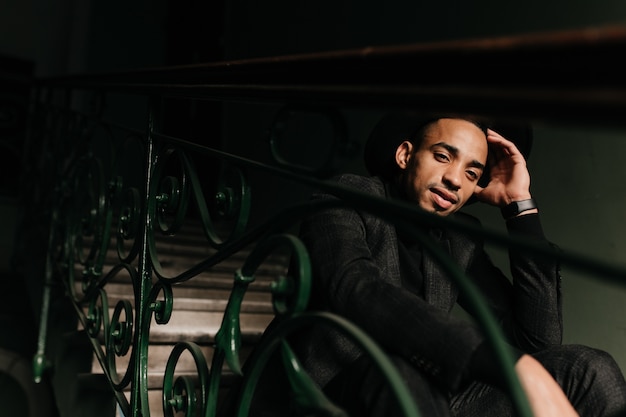 Interested african man chilling on stairs. Inspired guy in black attire sitting on steps and thinking about something.