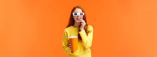 Free photo interested and amused smiling geeky redhead woman in yellow sweater watching movie in cinema wearing