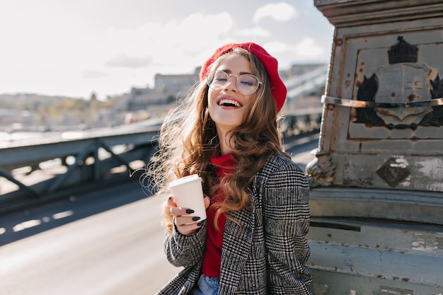 Interested caucasian girl in vintage outfit drinking coffee during trip around Europe